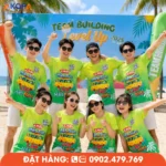Áo phông đồng phục nhóm màu xanh lá nổi bật với slogan “Chơi hết sức làm hết KPI”, chụp tại bãi biển trong hoạt động team building.