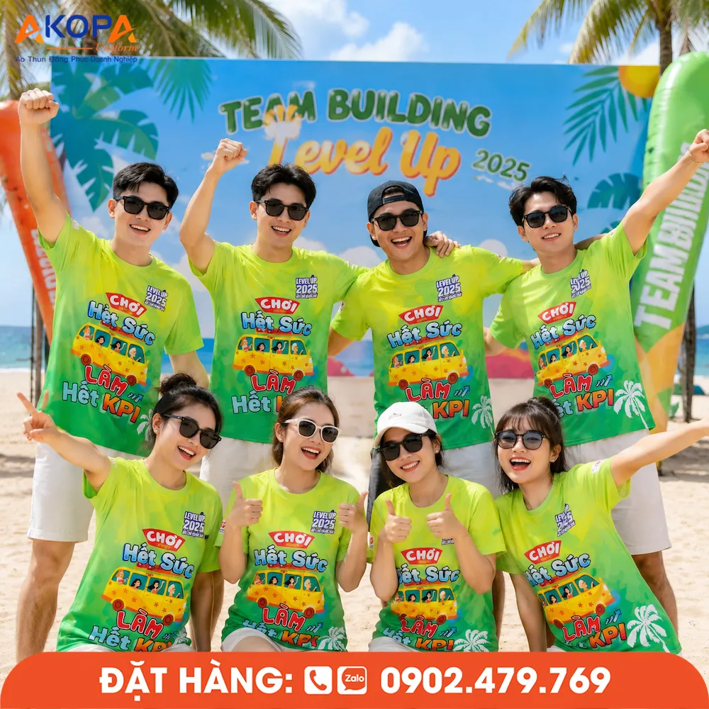 Áo phông đồng phục nhóm màu xanh lá nổi bật với slogan “Chơi hết sức làm hết KPI”, chụp tại bãi biển trong hoạt động team building.