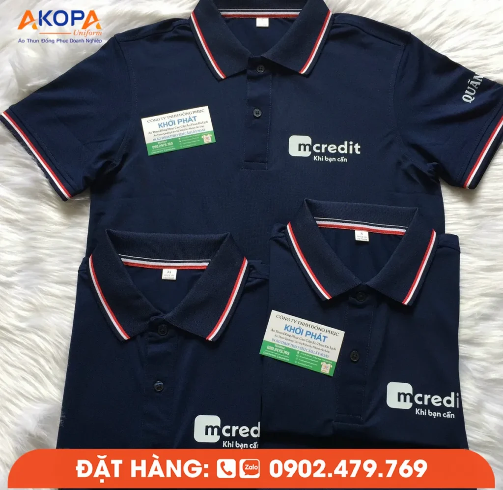 Áo polo Mcredit màu xanh navy được thiết kế theo phong cách chuyên nghiệp với logo thương hiệu trước ngực và chi tiết bo sọc đỏ trắng nổi bật ở cổ và tay áo