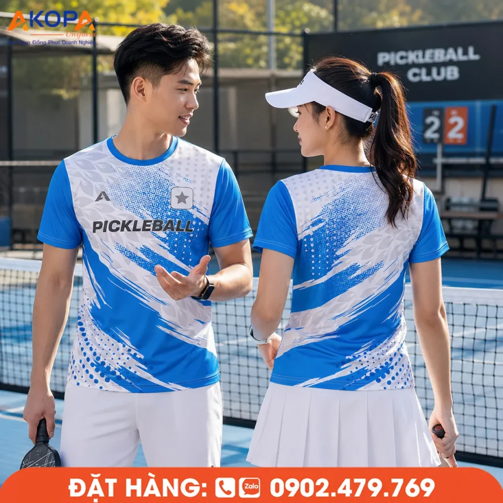 Áo đồng phục pickleball cổ tròn tông xanh dương phối trắng với họa tiết cọ sơn độc đáo, thiết kế trẻ trung, chất vải thoáng mát, thích hợp cho câu lạc bộ và đội thi đấu.