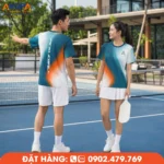 Áo đồng phục pickleball cổ tròn phối xanh teal cùng hiệu ứng chuyển màu cam nổi bật, thiết kế hiện đại với điểm nhấn chữ dọc mặt sau, mang đến phong cách năng động cho đội nhóm Pickleball.