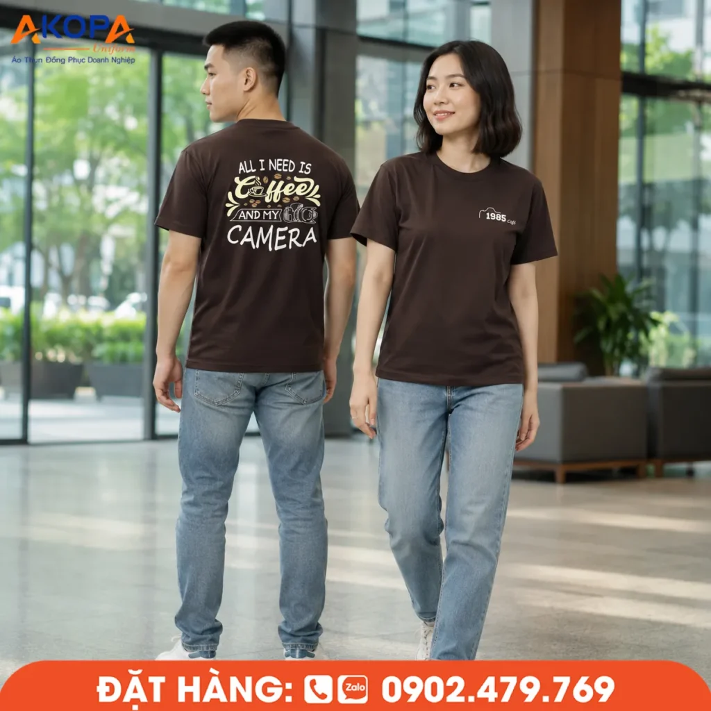 Áo thun đồng phục màu nâu cổ tròn, in logo trước ngực và họa tiết sau lưng nổi bật, phù hợp cho quán cà phê, cửa hàng, doanh nghiệp và đội nhóm.