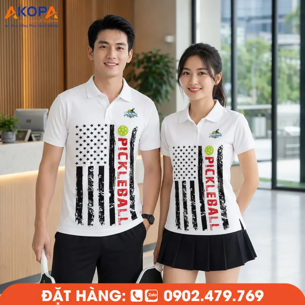 Áo Pickleball tông trắng phối họa tiết cờ và typography nổi bật, mang phong cách thể thao mạnh mẽ, hiện đại. Thiết kế form polo năng động, chất liệu co giãn, thấm hút tốt, phù hợp cho luyện tập, thi đấu và làm đồng phục câu lạc bộ Pickleball, giúp tạo dấu ấn chuyên nghiệp và khác biệt.